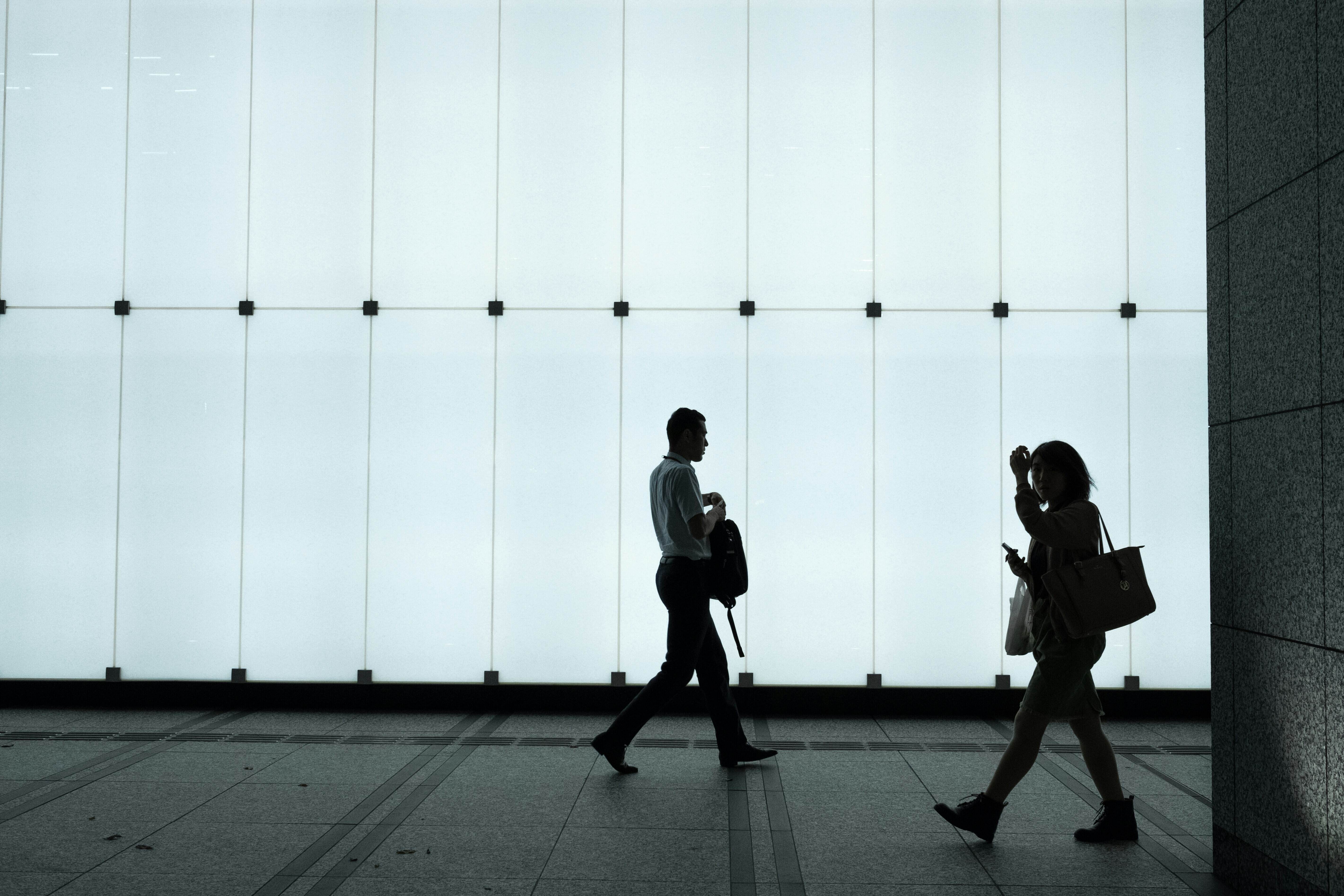 Two officer workers are seen walking past a lit-up office.